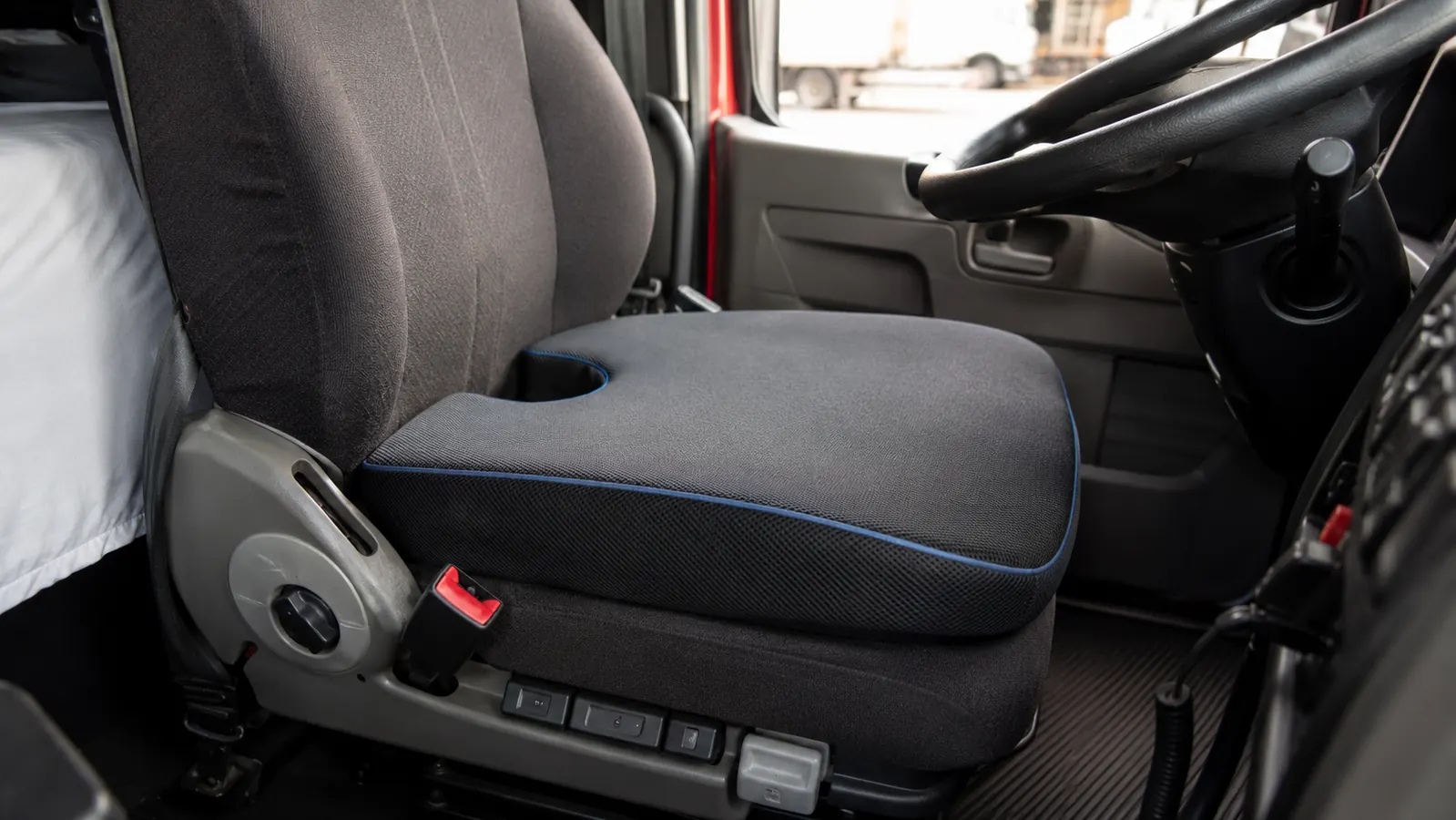 Truck driver adjusting position in cab seat with seat cushion, showing raised seating height near steering wheel