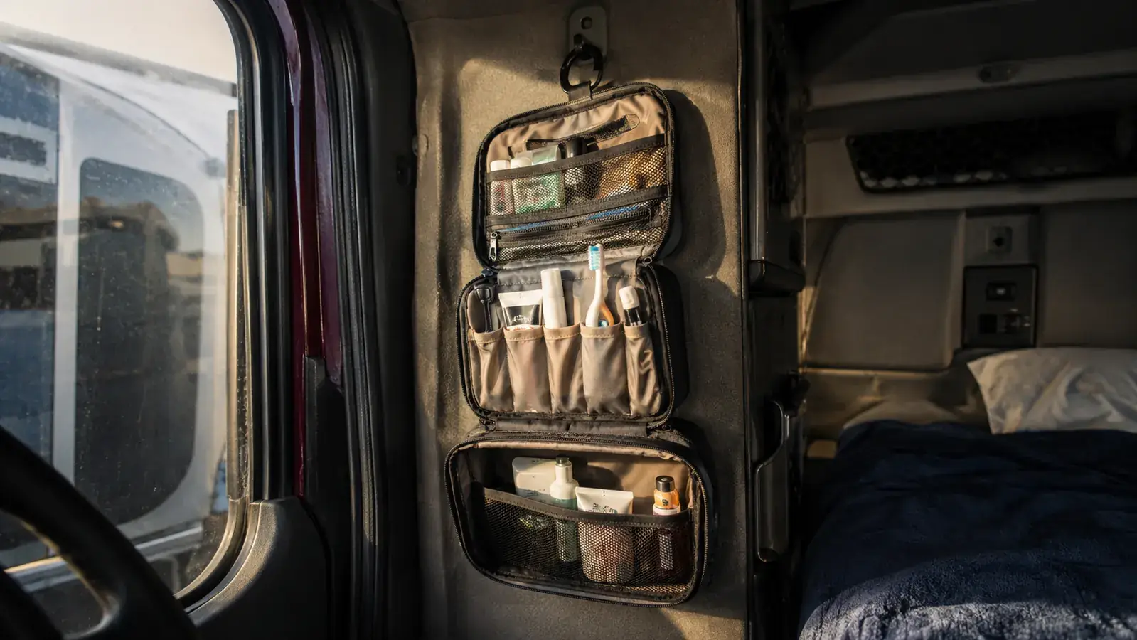 A trucker's hand hooking a toiletry bag onto a bathroom stall door in a truck stop shower room
